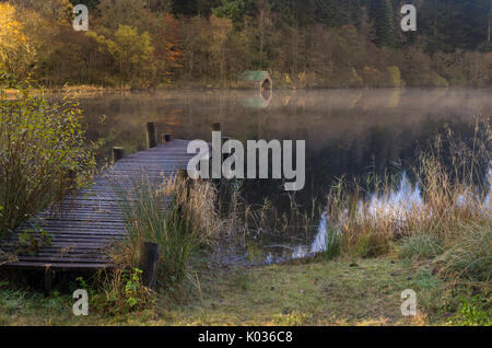 Wooden Jetty and boathouse on a misty morning with reflection, Loch Ard, Scotland Stock Photo