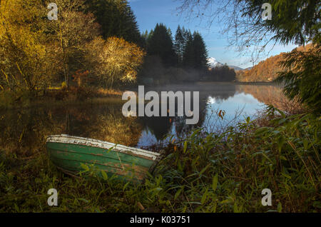 Wooden rowing boat at Milton Basin with reflection of landscape of trees and mountain, Loch Ard, Scotland Stock Photo