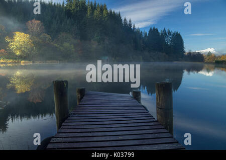 Wooden Jetty at Milton Basin with reflection of landscape of trees and mountain, Loch Ard, Scotland Stock Photo