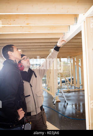 Carpenter Showing Wooden Roof To Colleague At Site Stock Photo