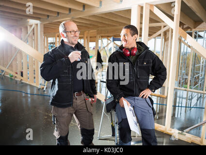 Colleagues With Plan And Coffee Cup Smiling At Construction Site Stock Photo