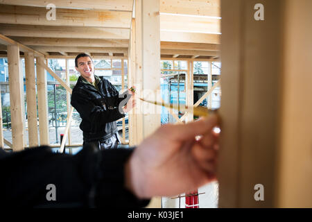 Happy Carpenter Measuring Wood With Help Of Colleague At Site Stock Photo