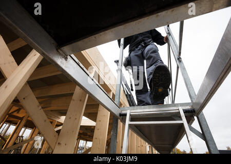 Male Carpenter Moving Down Ladder At Incomplete Building Stock Photo