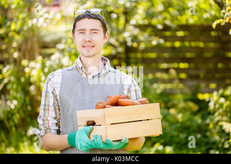Photo of guy with gloves holding box of carrots in hands Stock Photo