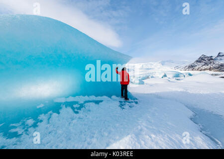 Fjallsarlon glacier lagoon, East Iceland, Iceland. Man with red coat admiring the view of the frozen lagoon in winter (MR). Stock Photo