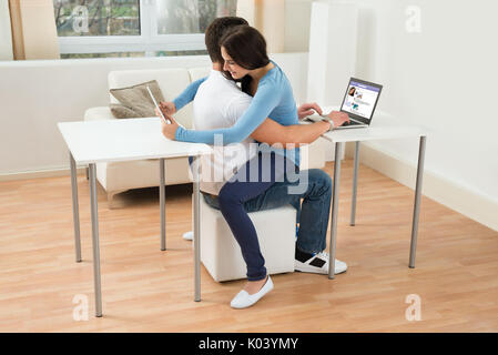 Portrait Of A Young Couple At Home Using Digital Tablet And Laptop Stock Photo