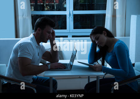 Bored Young Couple Using Digital Tablet And Laptop At Night Stock Photo