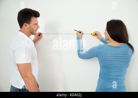 Close-up Of Young Couple Measuring Wall With Measurement Tape And Pencil Stock Photo