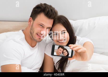 Happy Young Couple Lying On Bed Taking A Selfie With Mobile Phone Stock Photo