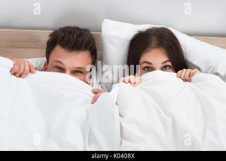 Portrait Of Young Couple Hiding Face With Blanket In Bedroom Stock Photo