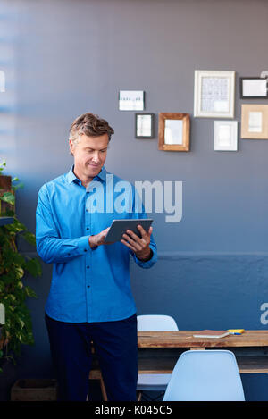 Smiling businessman standing in an office using a digital tablet Stock Photo