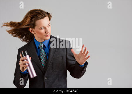 A portrait of a handsome long-haired man in suit holding a bottle of hair spray. Stock Photo