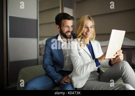 Businessman and businesswoman sitting on bed and using tablet Stock Photo
