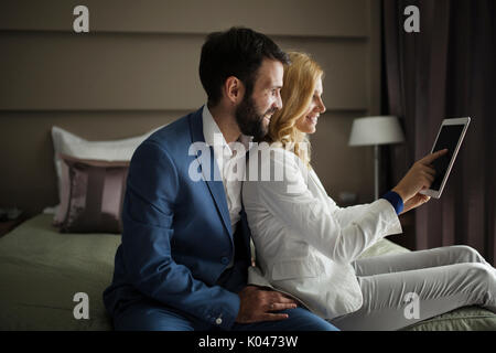 Businessman and businesswoman sitting on bed and using tablet Stock Photo