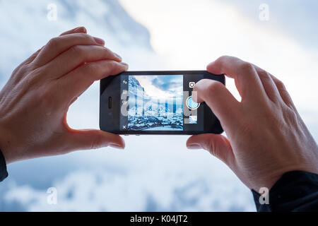 GRINDELWALD, SWITZERLAND - FEBRUARY 4, 2014: Woman taking a photograph of mountains using the Instagram App on an Apple iPhone. Instagram allows users Stock Photo