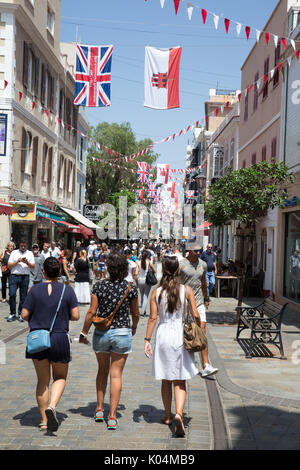 People strolling along Main Street in the UK dependency of Gibraltar with the Union Jack and the flag of Gibraltar in the background Stock Photo