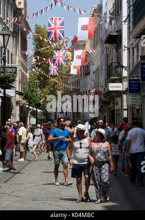 People strolling along Main Street in the UK dependency of Gibraltar with the Union Jack and the flag of Gibraltar in the background Stock Photo