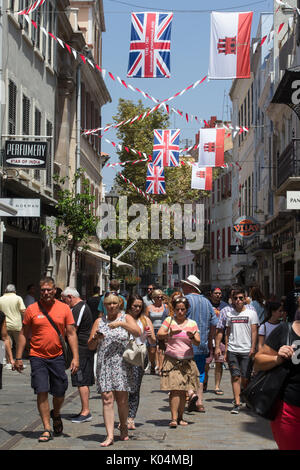 People strolling along Main Street in the UK dependency of Gibraltar with the Union Jack and the flag of Gibraltar in the background Stock Photo