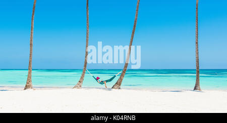 Juanillo Beach (playa Juanillo), Punta Cana, Dominican Republic. Woman relaxing on a hammock on a palm-fringed beach (MR). Stock Photo