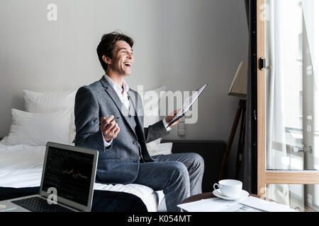 Young laughing male lawyer reviewing some documents and contracts in a hotel room during a business trip Stock Photo