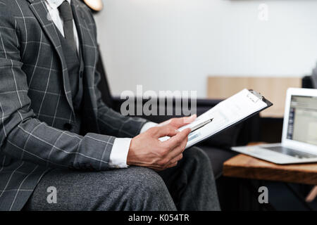 Cropped image of a man in suit analyzing documents while sitting on a couch Stock Photo