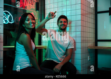 Image of young multiethnic loving couple sitting in cafe looking aside. Stock Photo