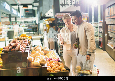 Young couple with cell phone grocery shopping at market Stock Photo