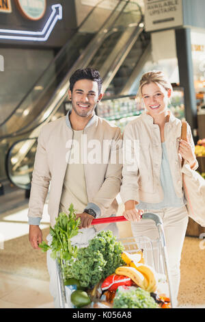 Portrait smiling young couple with shopping cart grocery shopping in market Stock Photo