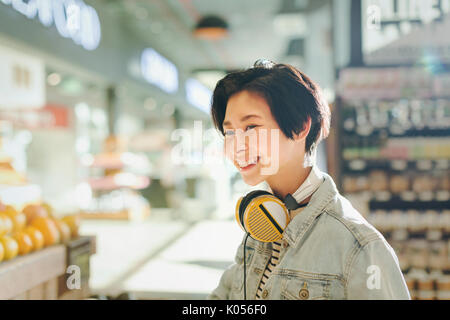 Smiling young woman with headphones grocery shopping in market Stock Photo