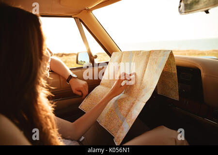 Young couple holding a map while sitting together on a front seat inside a car and hugging Stock Photo