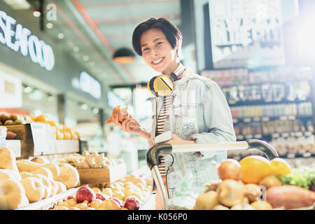 Portrait smiling young woman with headphones grocery shopping in market Stock Photo