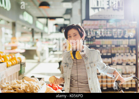 Portrait smiling, confident young woman with headphones grocery shopping in market Stock Photo
