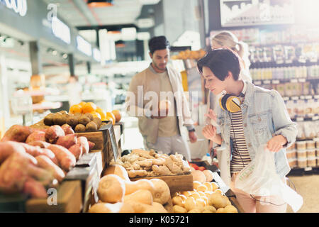 Young woman with headphones grocery shopping, browsing produce in market Stock Photo