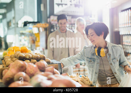 Young woman with headphones grocery shopping, browsing produce in market Stock Photo