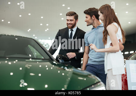 Handsome young car salesman telling a young couple about the features of the car at the dealership Stock Photo