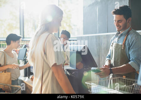 Male cashier helping female shopper at grocery store checkout Stock Photo