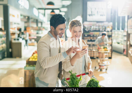 Young couple using cell phone, grocery shopping in grocery store market Stock Photo