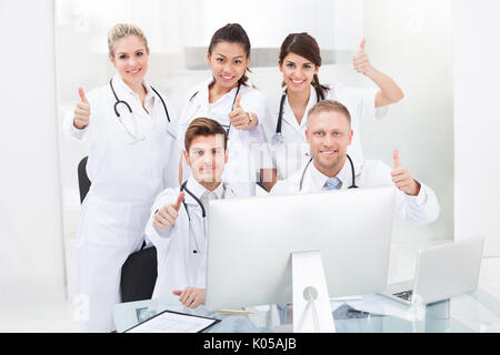 Portrait of confident doctors gesturing thumbs up at desk in clinic Stock Photo
