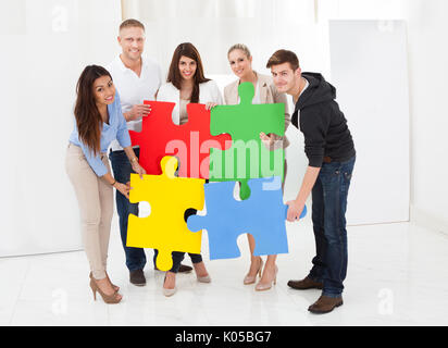 Full length portrait of confident businesspeople joining puzzle pieces in office Stock Photo