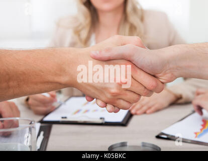 Cropped image of businessmen shaking hands at desk in office Stock Photo