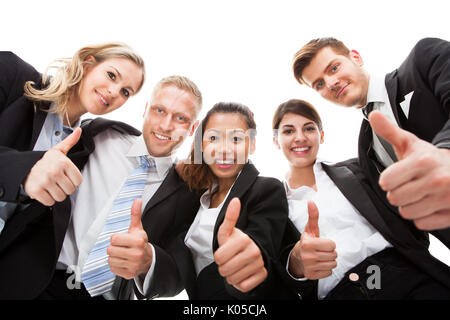 Low angle portrait of business people gesturing thumbs up against white background Stock Photo