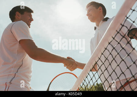 Young male tennis players handshaking in sportsmanship at net Stock Photo