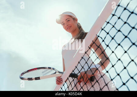 Portrait smiling, confident female tennis player holding tennis racket at net below sunny sky Stock Photo
