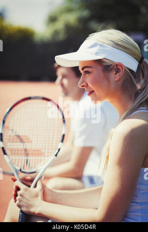 Smiling, confident female tennis player holding racket on sunny tennis court Stock Photo