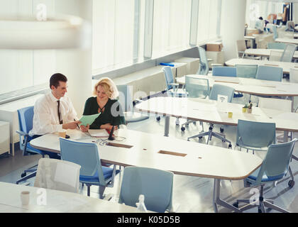 Businessman and businesswoman discussing paperwork at table in shared workspace Stock Photo