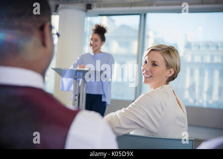 Smiling businesswoman turning and listening to businessman in conference audience Stock Photo