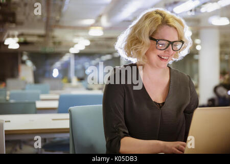 Smiling businesswoman working late at laptop in dark office Stock Photo