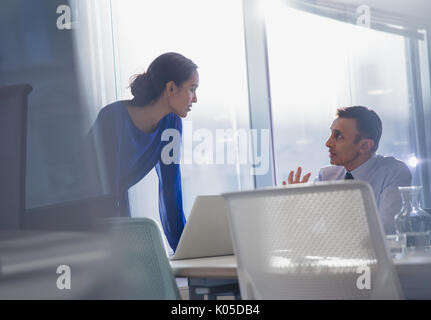 Businessman and businesswoman using laptop, talking in office Stock Photo