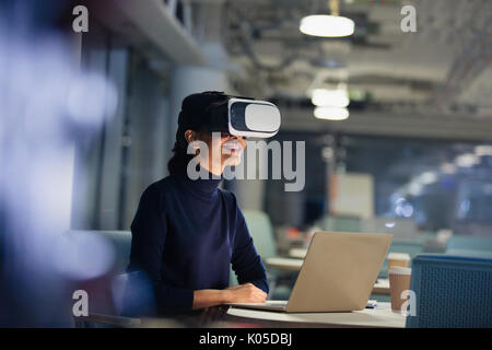 Businesswoman using virtual reality simulator at laptop in dark office Stock Photo