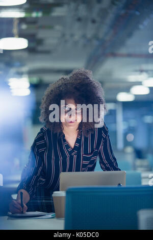 Portrait smiling confident businesswoman working late at laptop in dark office Stock Photo